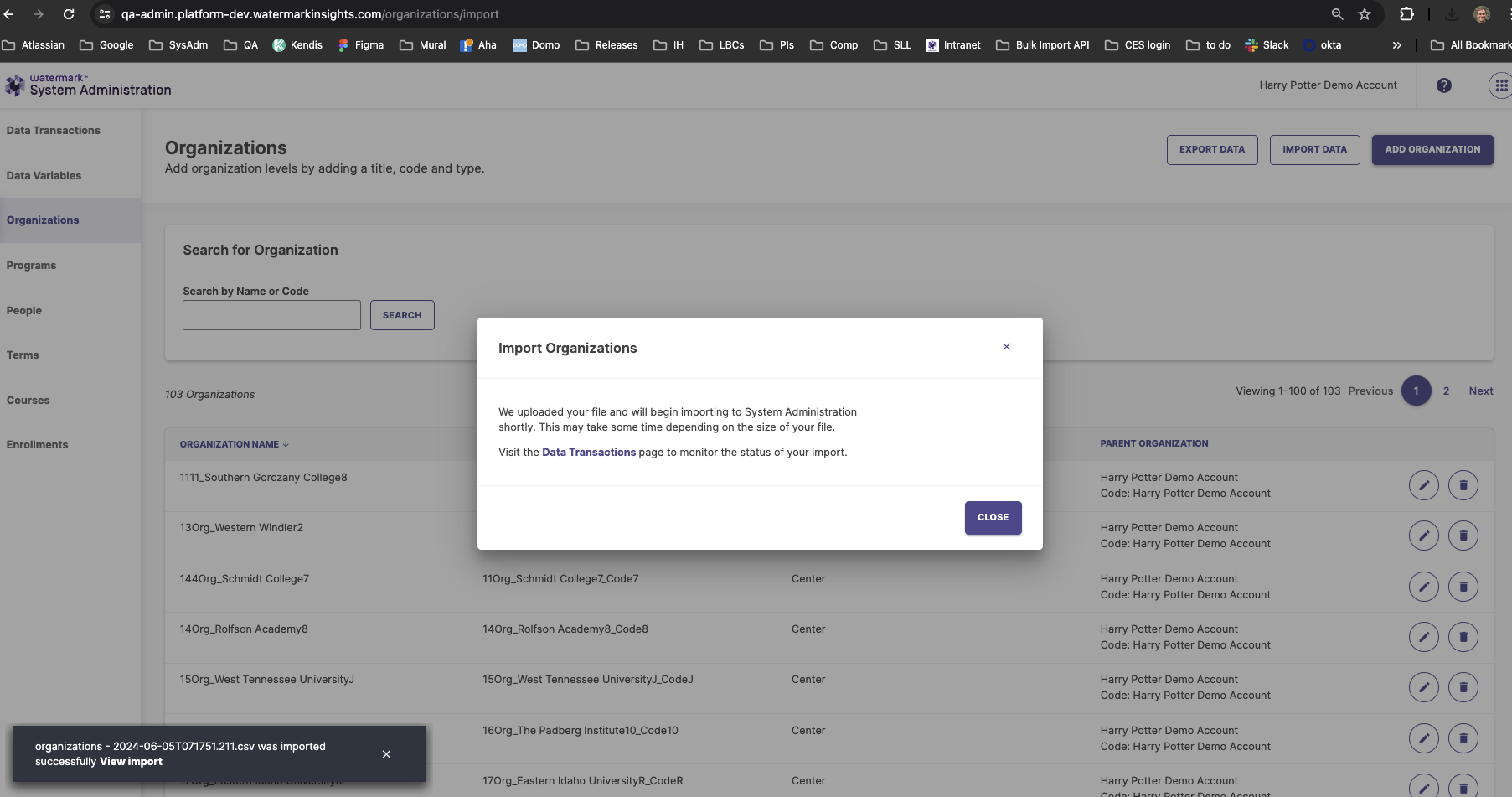 The System Administration interface showing the Organizations page with an Import Organizations confirmation modal open. The modal informing the user that the uploaded file is beginning to process and providing a Close button. The background showing the organization list and related management options within System Administration.